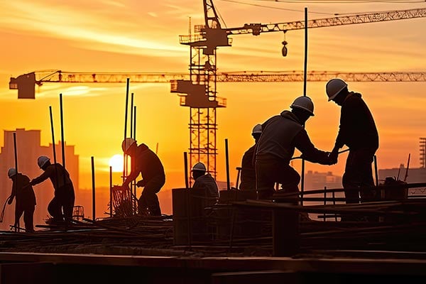 Silhouettes of construction site workers at sunset.