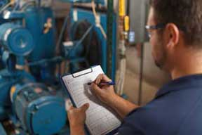 Worker with clipboard performs a check on industrial equipment.