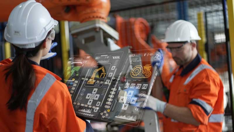Workers in PPE and hardhats operating a machine control panel.