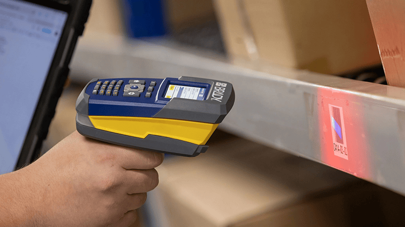 Worker holds a Brady handheld scanner and scans a shelf. 