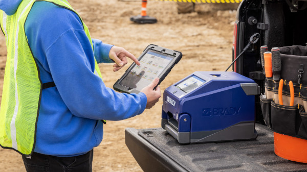 Person using a tablet to connect to a Brady i4311 label printer at a jobsite.