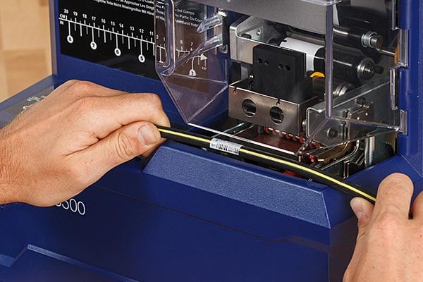 Technician feeds a cable into a Brady A6500 Wrap Printer.