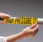 A worker applies a self adhesive pipe marker to a shiny metal pipe